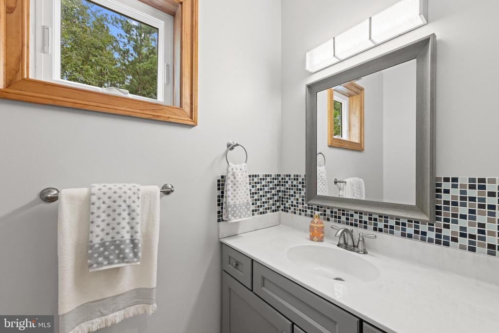 Bathroom vanity with a large mirror, mosaic tile backsplash, and wood-trimmed window.