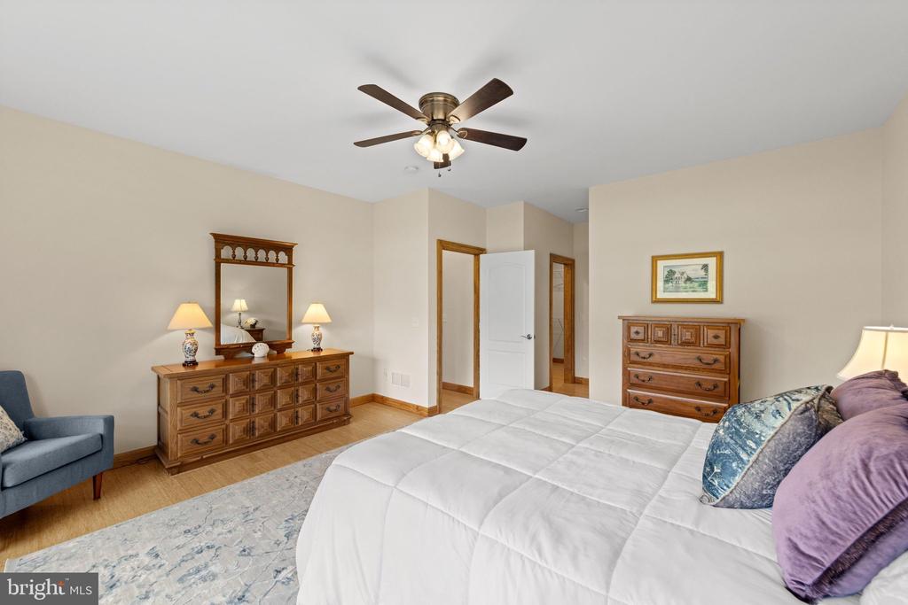 Furnished bedroom with a white bed, wood dressers and mirror, ceiling fan, and blue armchair.