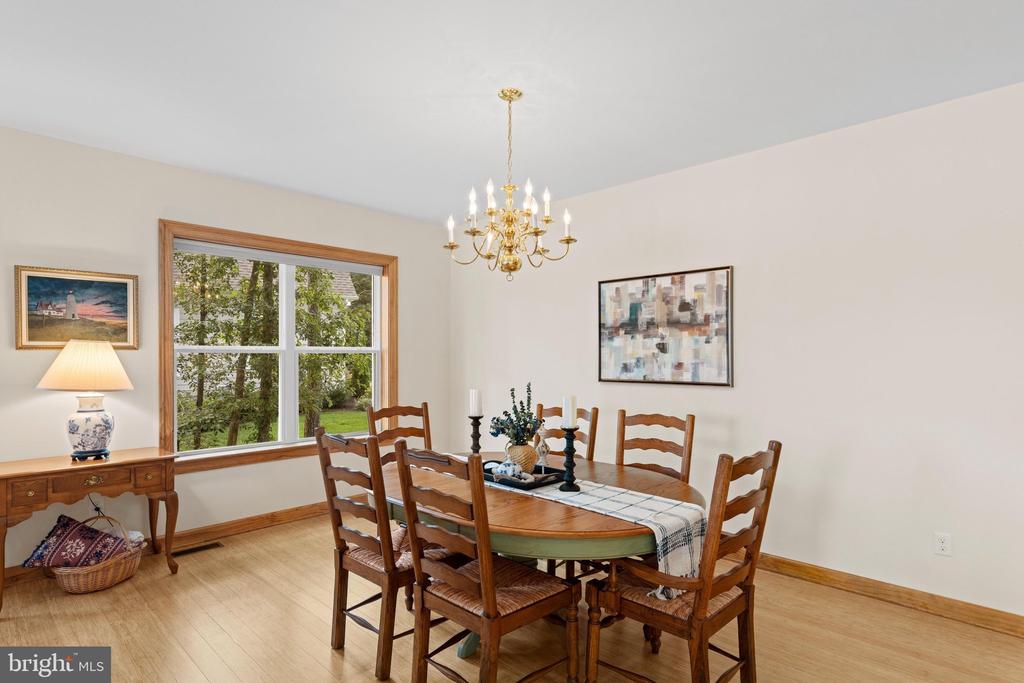 Dining room with an oval wooden table, chandelier, and large window overlooking greenery.