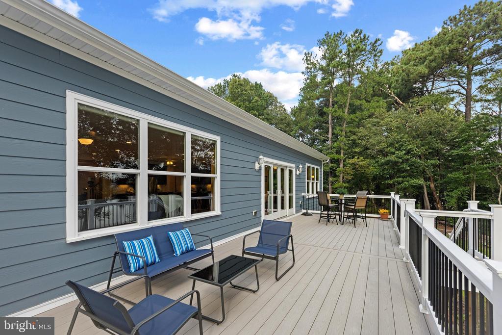 Spacious deck with blue lounge chairs, dining set, white railings, and surrounding trees.