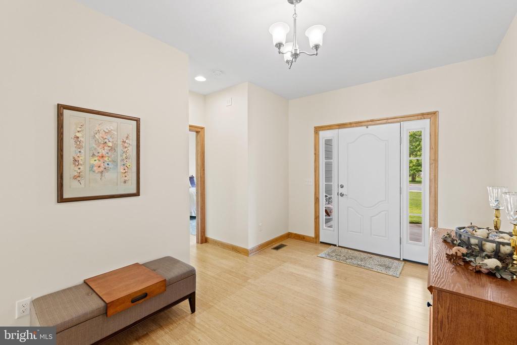 Entry foyer with a white front door and sidelights, light wood flooring, chandelier, and bench.