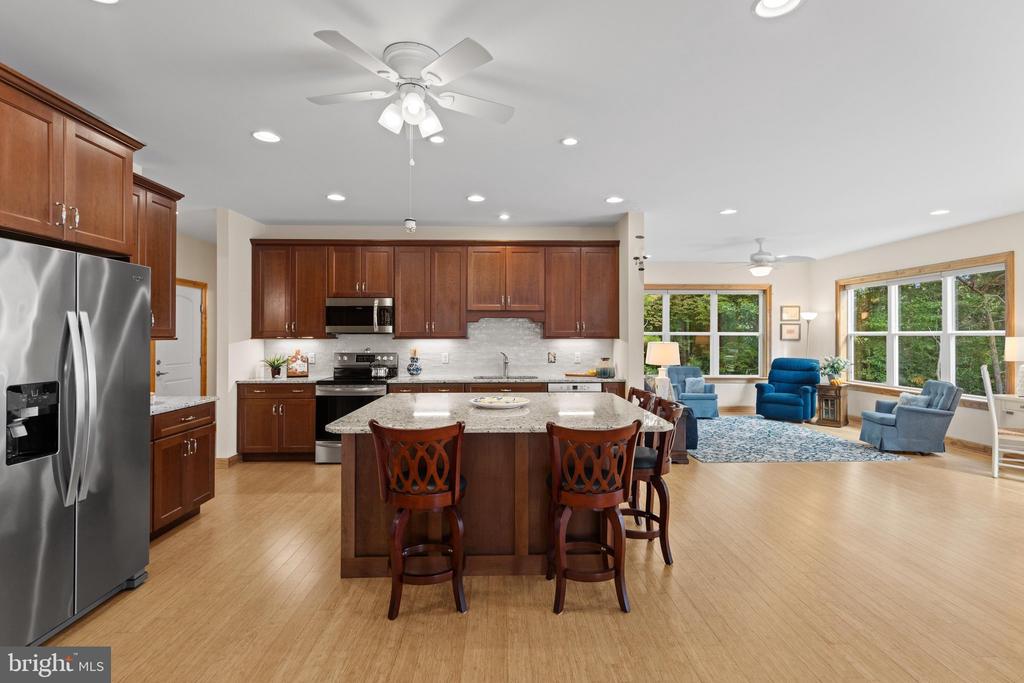 Open kitchen with dark wood cabinets, stainless steel appliances, and a granite island adjoining a bright living area.