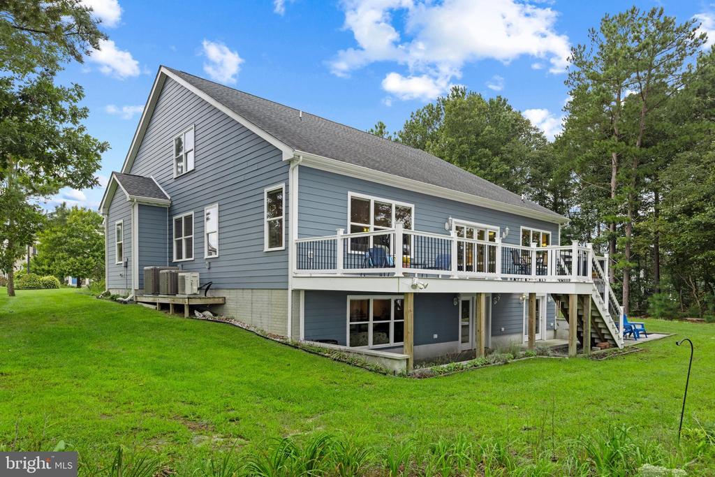 Blue-gray two-story home with a raised deck, outdoor furniture, and a spacious green lawn.