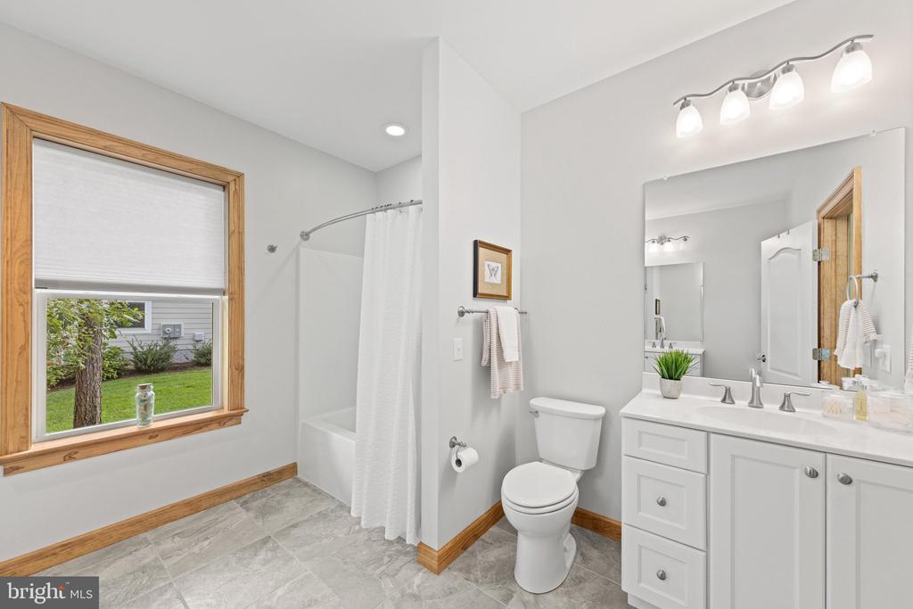 Bathroom with a white double vanity, gray tile floor, and wood-trimmed window overlooking a yard.