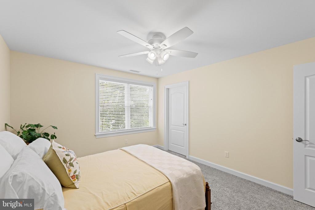 Bedroom with pale yellow bedding, a window with white blinds, and a white ceiling fan.