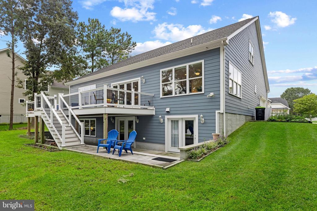 Blue-gray house with an elevated deck, white stairs, and a patio with blue Adirondack chairs.