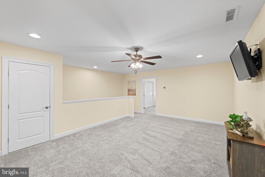 Carpeted room with a ceiling fan, wall-mounted television, and pale yellow walls.