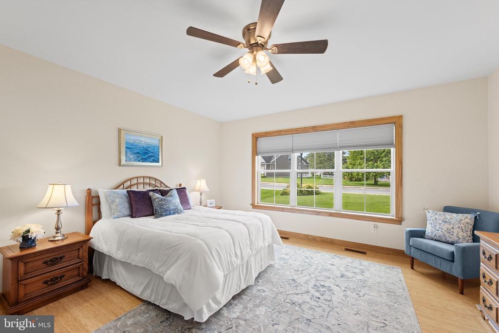 Staged bedroom with a large bed, wood nightstand, blue chair, and wide window overlooking a green lawn.