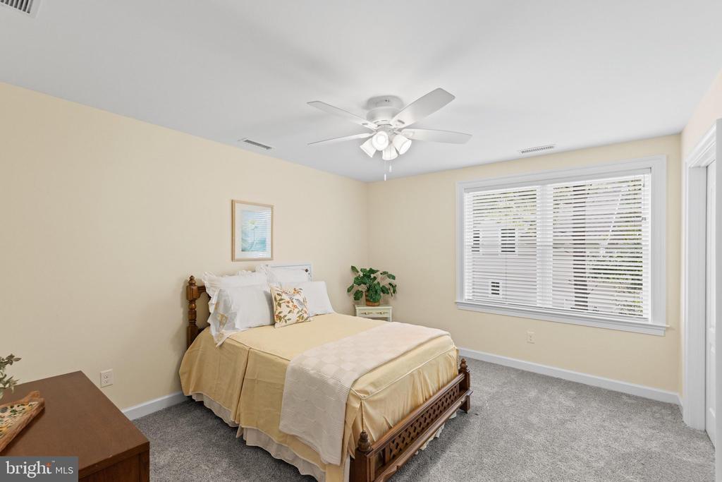 Bedroom with a carved wooden bed, cream bedding, gray carpet, and a large window with blinds.