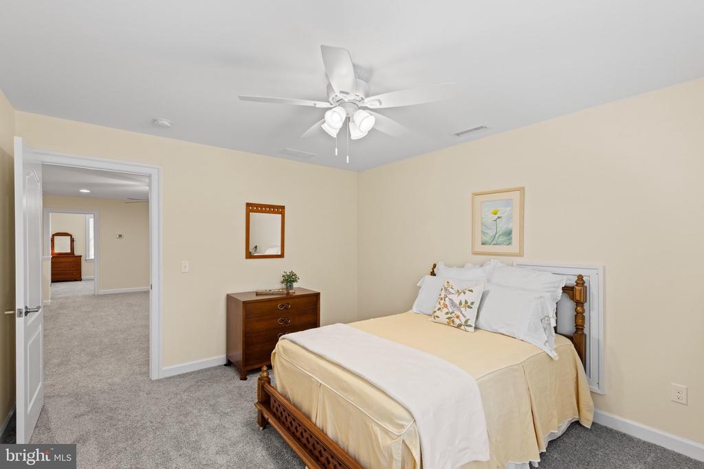 Bedroom with cream bedding, a wooden bed, gray carpet, and an open doorway to the hall.
