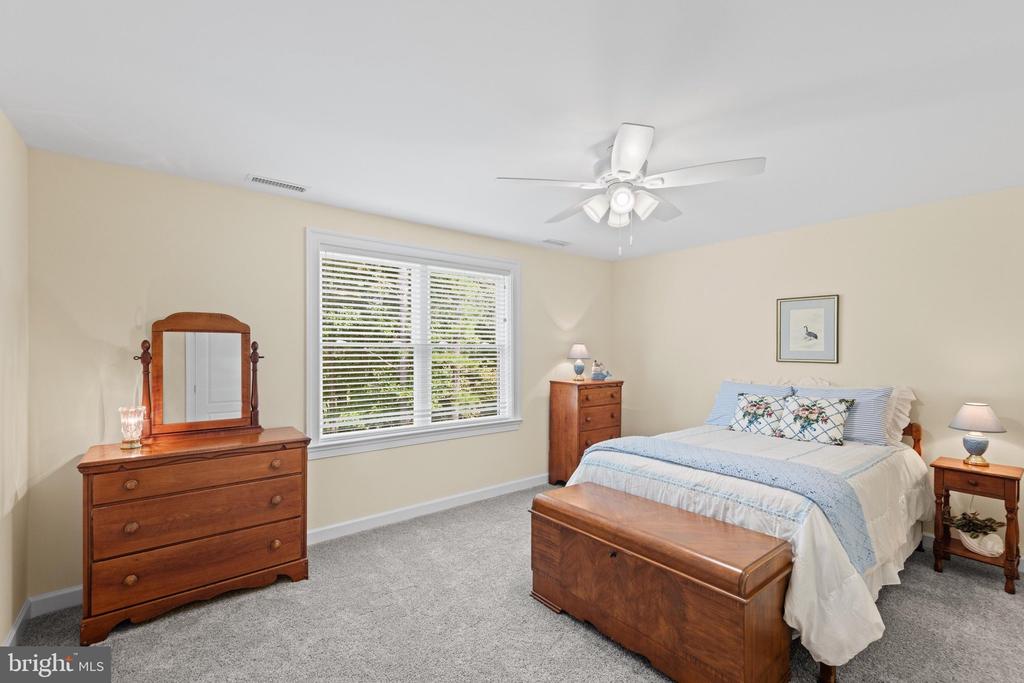 Bedroom with large window, wooden furniture, and a chest at the foot of the bed.