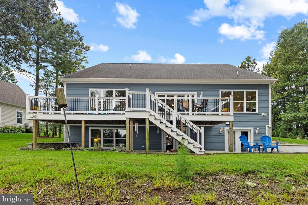 Blue-sided home with a raised deck, white stairs, and blue chairs beside the lawn.