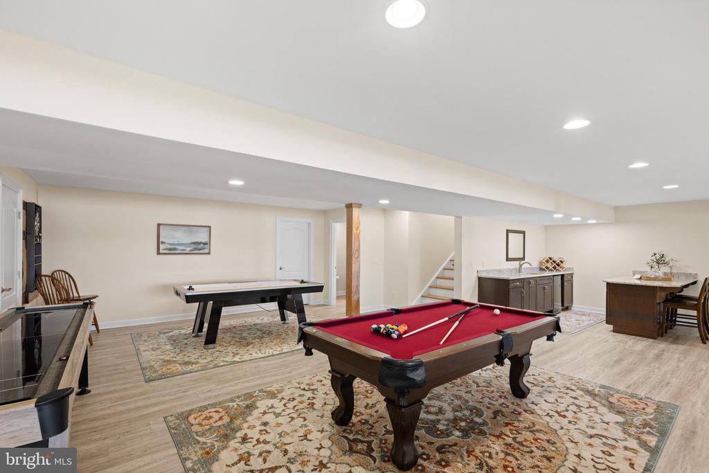 Finished basement game room with a red pool table, shuffleboard table, and kitchenette.