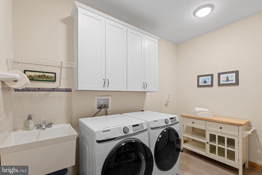 Laundry room with front-loading washer and dryer, utility sink, and white storage cabinets.