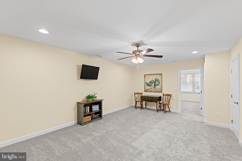 Carpeted room with a ceiling fan, wall-mounted television, bookcase, and small table with two chairs.