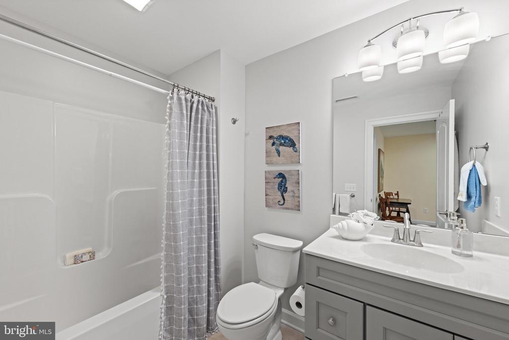 Bathroom with a tub-shower, gray vanity, wide mirror, and two coastal-themed pictures.