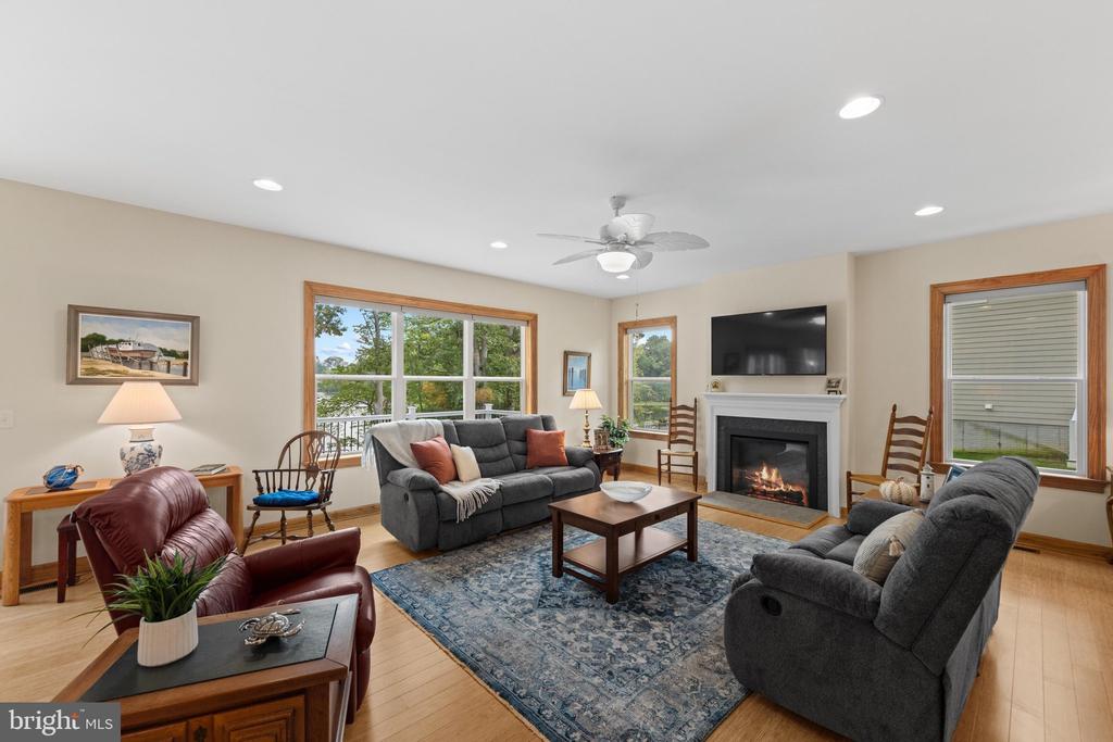 Living room with gray sofas, a fireplace, and large windows overlooking trees.