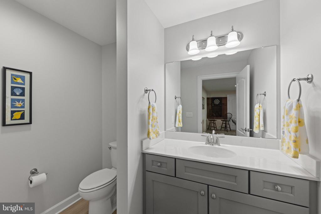 Bathroom with a gray vanity and large mirror, yellow-and-white towels, and framed coastal artwork.