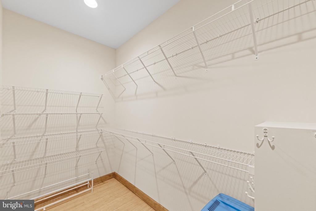 Walk-in closet with white wire shelving on three walls and light wood flooring.