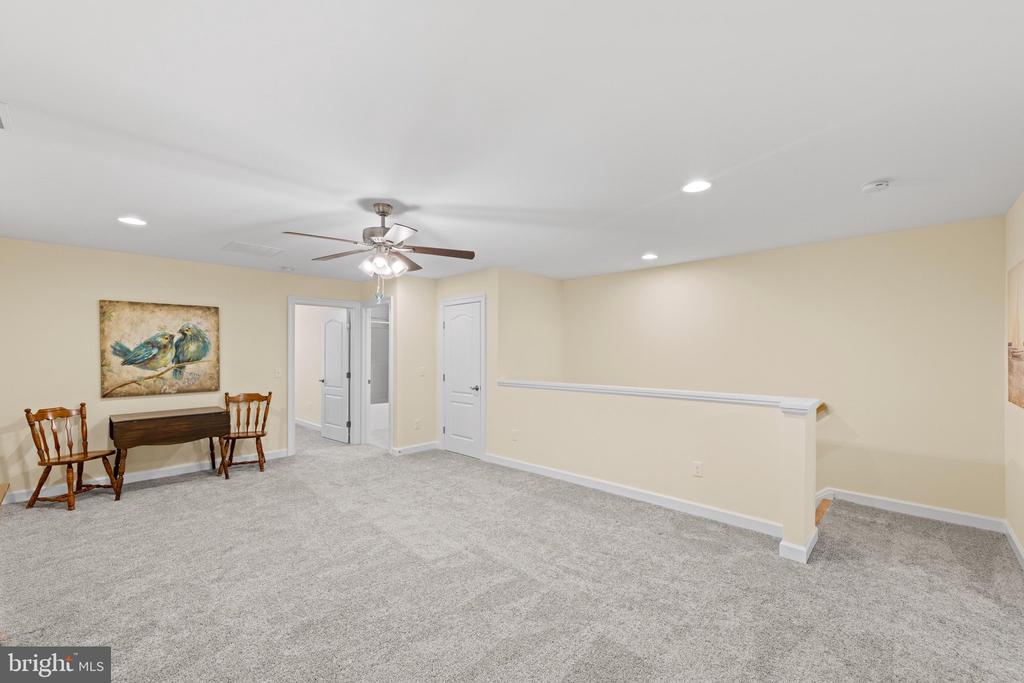 Carpeted room with a ceiling fan, small wooden table and chairs, and railing beside a stair opening.