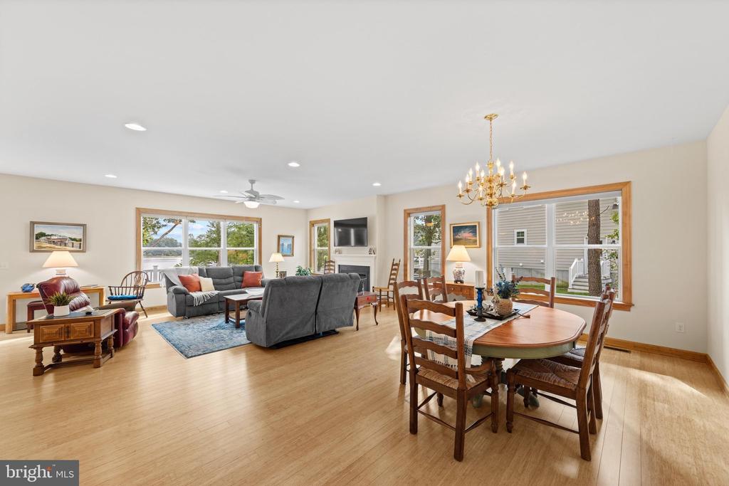 Open living and dining room with wood floors, gray sofas, and large windows overlooking water.