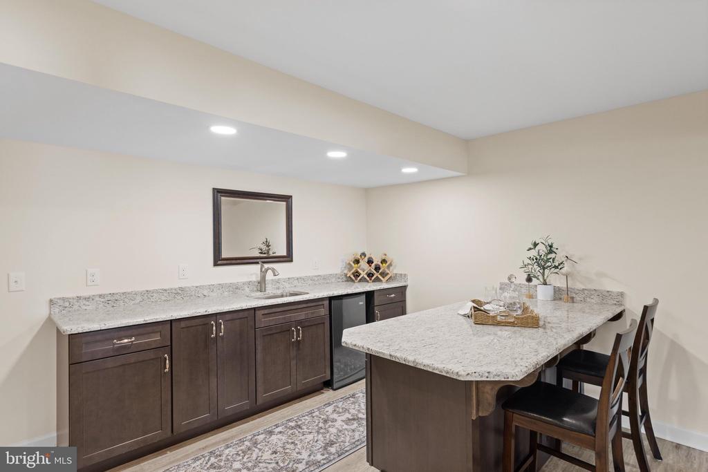 Basement wet bar with granite counters, dark wood cabinets, sink, beverage cooler, and island seating.