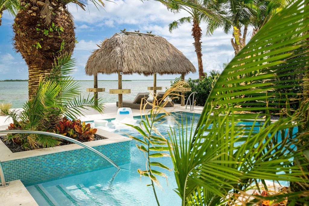 Tropical pool beside the shoreline, with a thatched gazebo and palms.