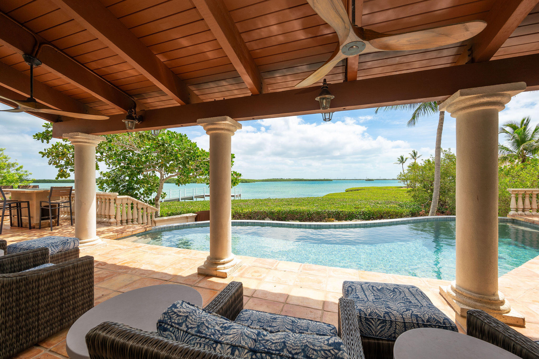Covered patio with wicker seating overlooks a swimming pool and turquoise ocean.