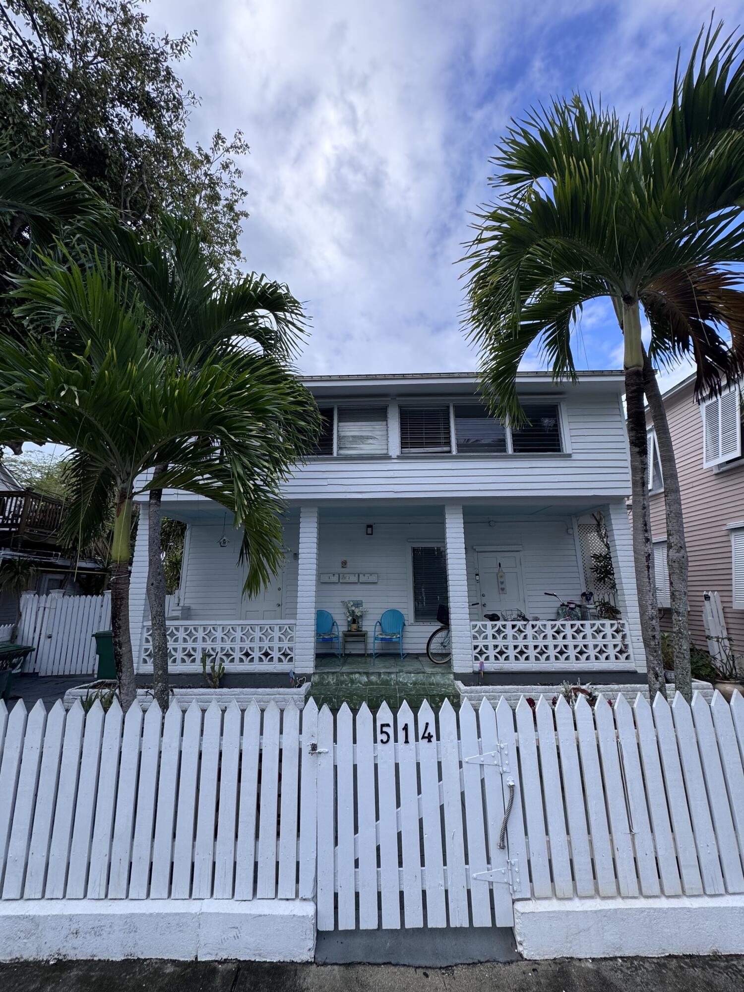 White two-story Key West house behind a picket fence marked 514, framed by palm trees.