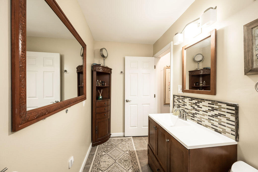 Bathroom with a dark wood vanity, mosaic tile backsplash, and ornate framed mirrors.