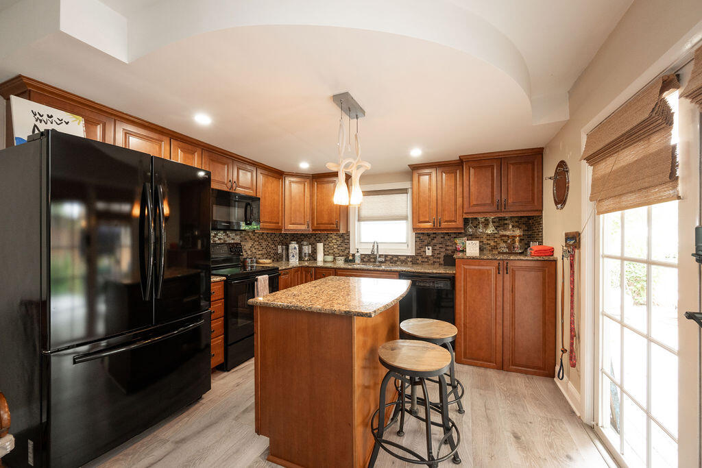 Kitchen with a granite-topped island, warm wood cabinetry, black appliances, and a glass-paneled door.