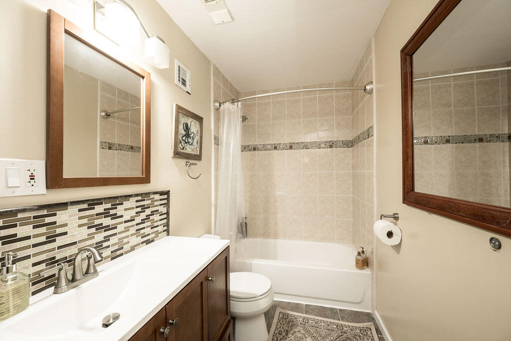 Bathroom with a tiled tub surround, dark wood vanity, mosaic backsplash, and large framed mirrors.