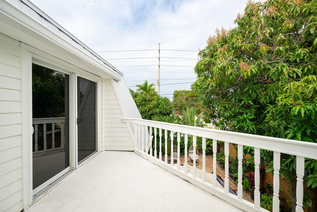 White balcony overlooking tropical trees and a landscaped yard.