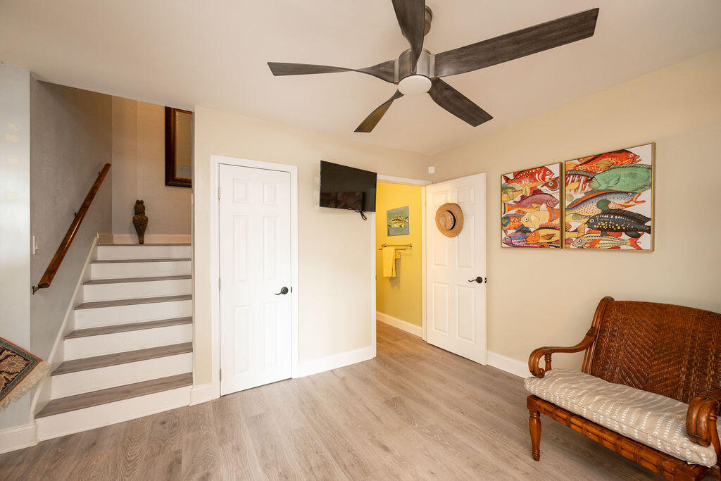 Furnished room with a staircase, wicker armchair, colorful fish artwork, and an open doorway to a yellow bathroom.