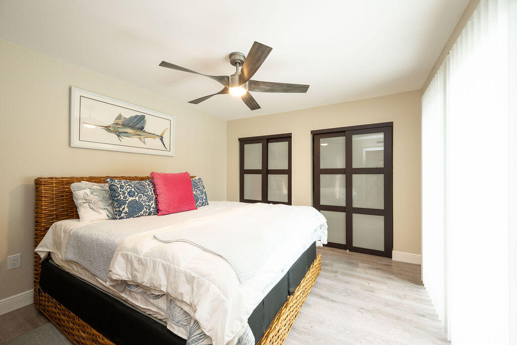 Bedroom with a wicker bed, white bedding, dark-framed sliding doors, and a ceiling fan.