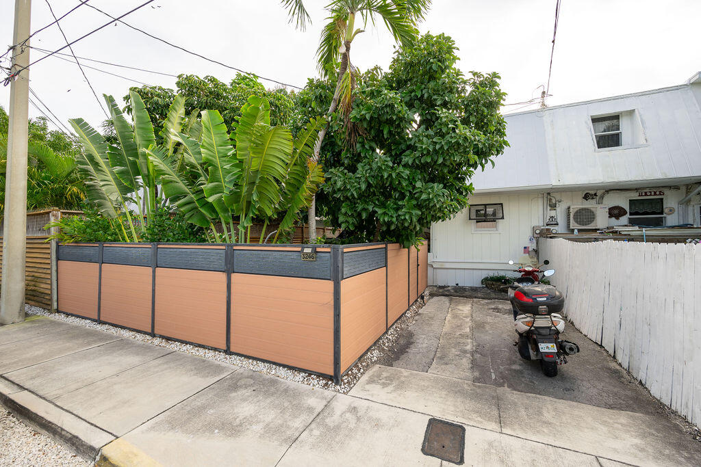 Property exterior with a peach-and-gray privacy fence, tropical foliage, and a scooter beside the driveway.