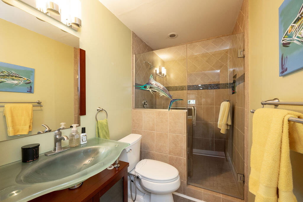 Bathroom with a beige-tiled glass shower, green glass sink, and fish artwork.