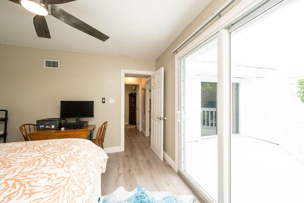 Bedroom with a patterned bedspread, ceiling fan, and sliding glass doors to a bright outdoor area.