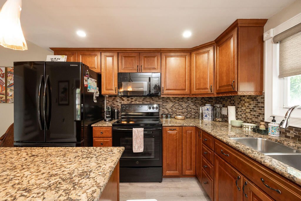 Kitchen with wood cabinetry, granite counters, mosaic backsplash, and black appliances.