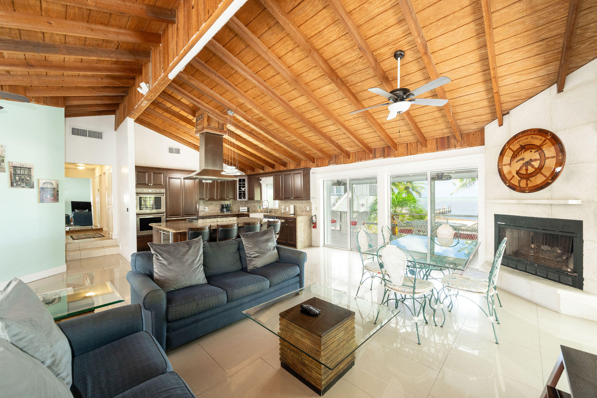 Open-plan living room and kitchen with a vaulted wood ceiling, fireplace, and water views.
