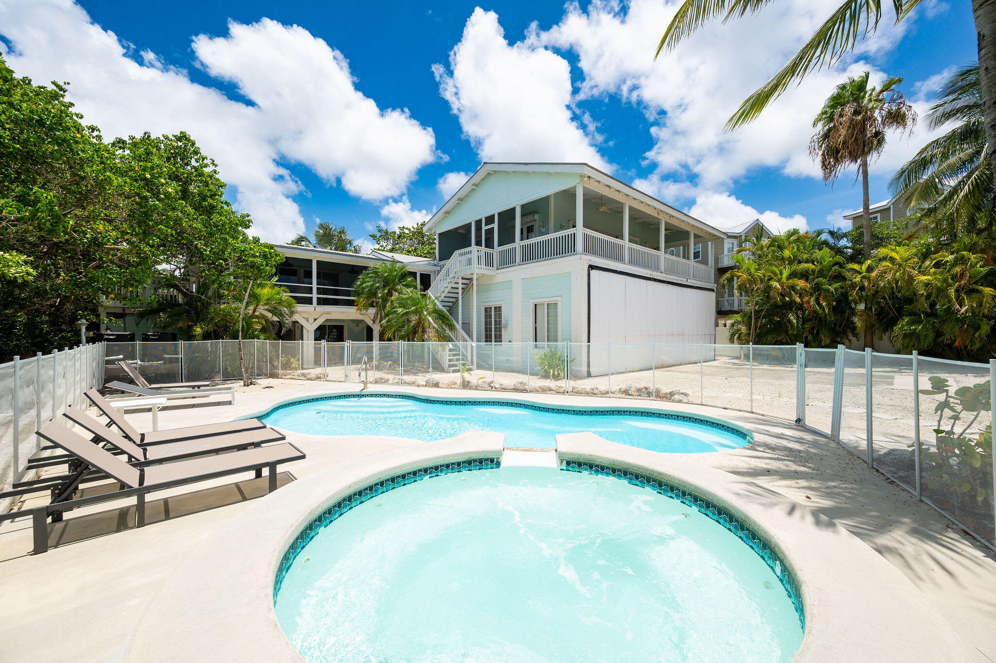 Aqua coastal home with an elevated porch behind a fenced pool and spa.