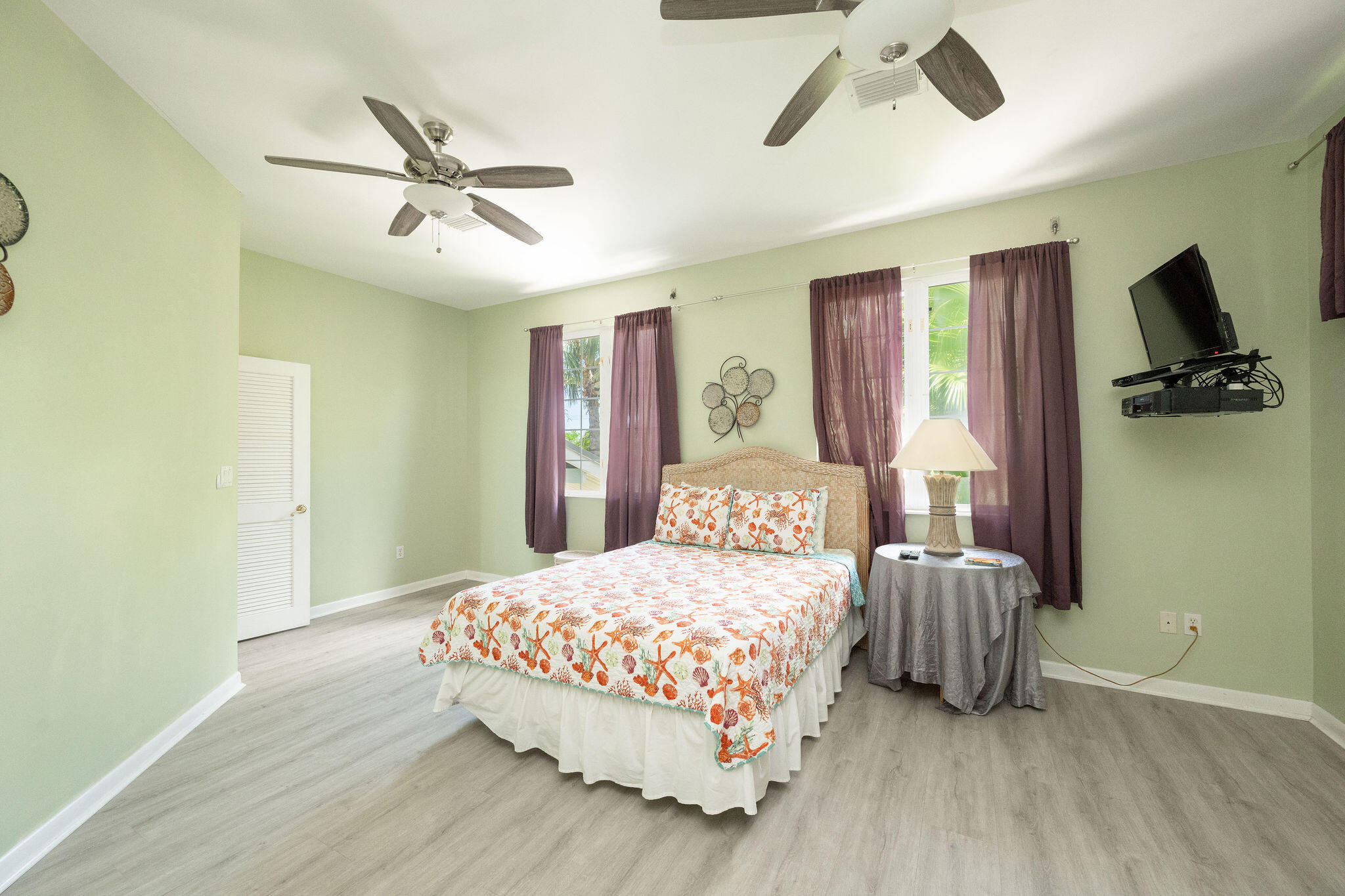 Bedroom with seashell-patterned bedding, purple curtains, and two ceiling fans.