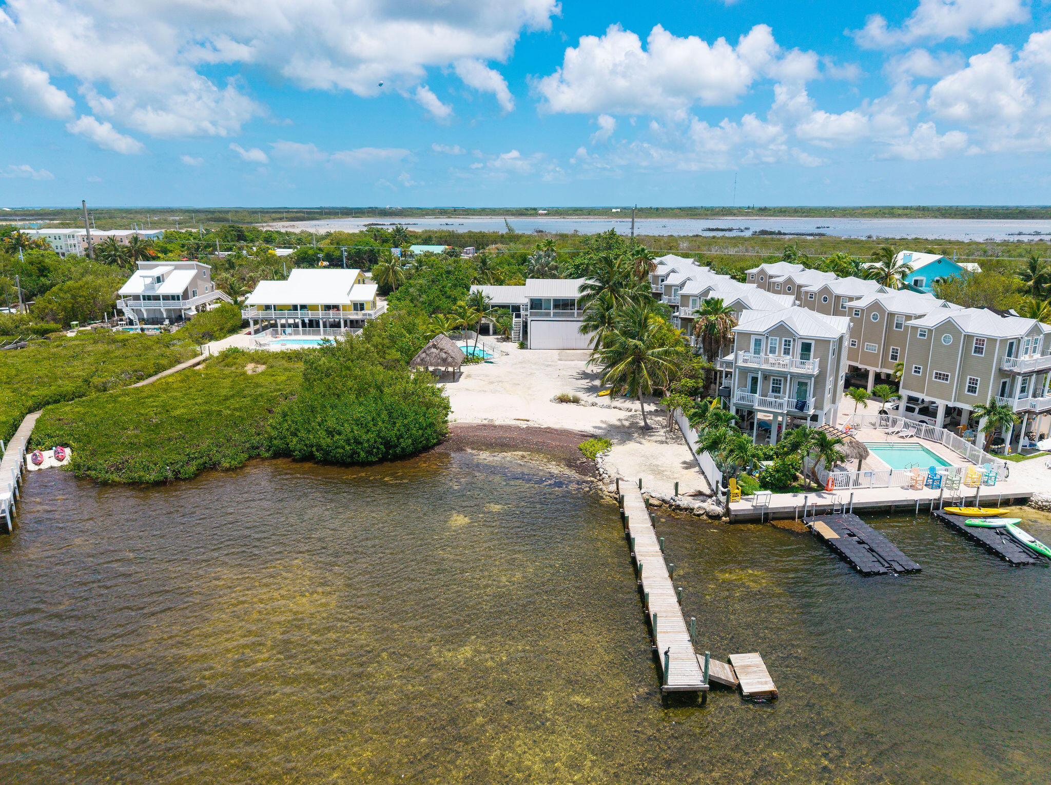 Aerial view of waterfront homes, pools, and docks along a shallow Florida Keys shoreline.