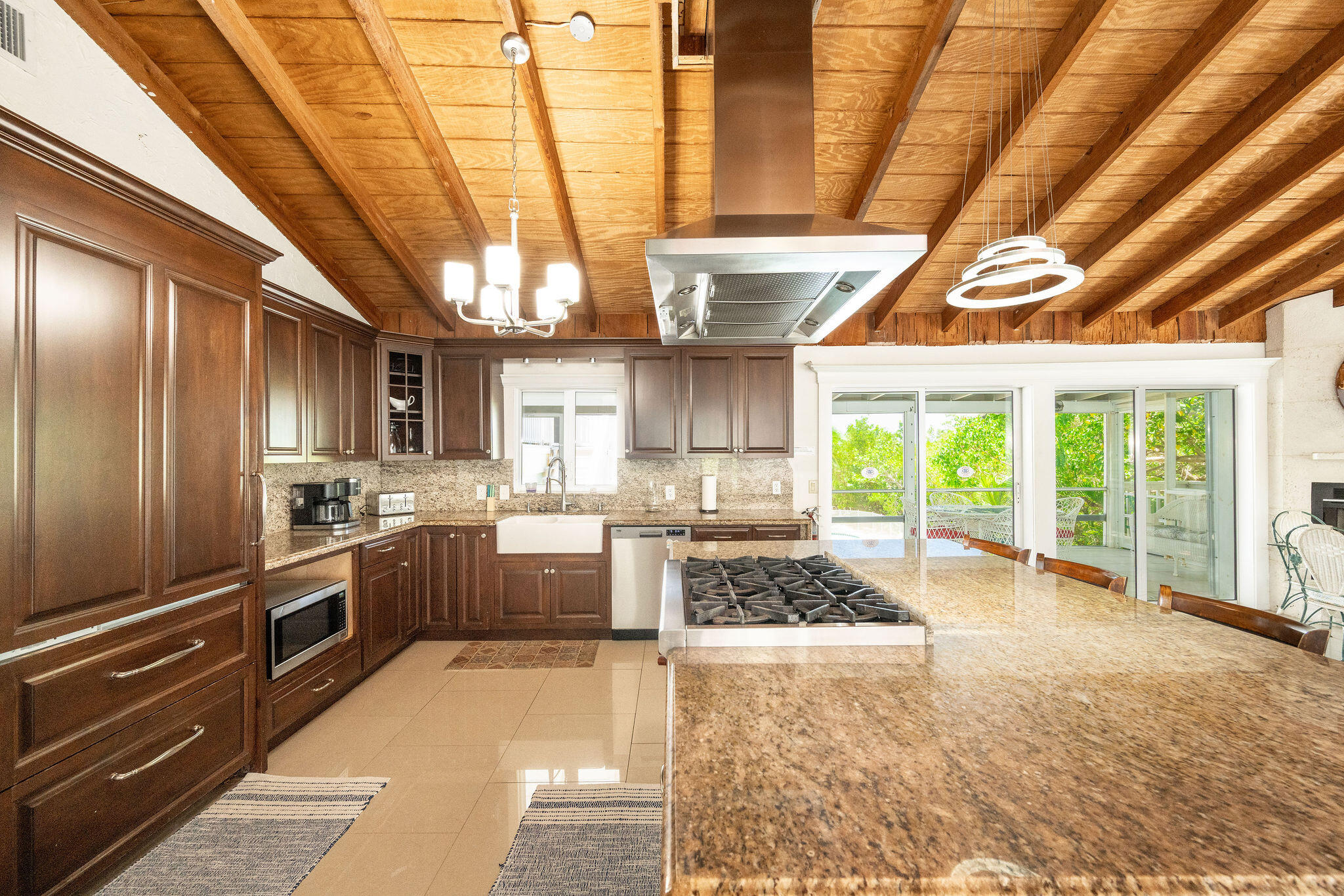 Kitchen with dark wood cabinets, granite island and gas cooktop beneath an exposed-beam ceiling.
