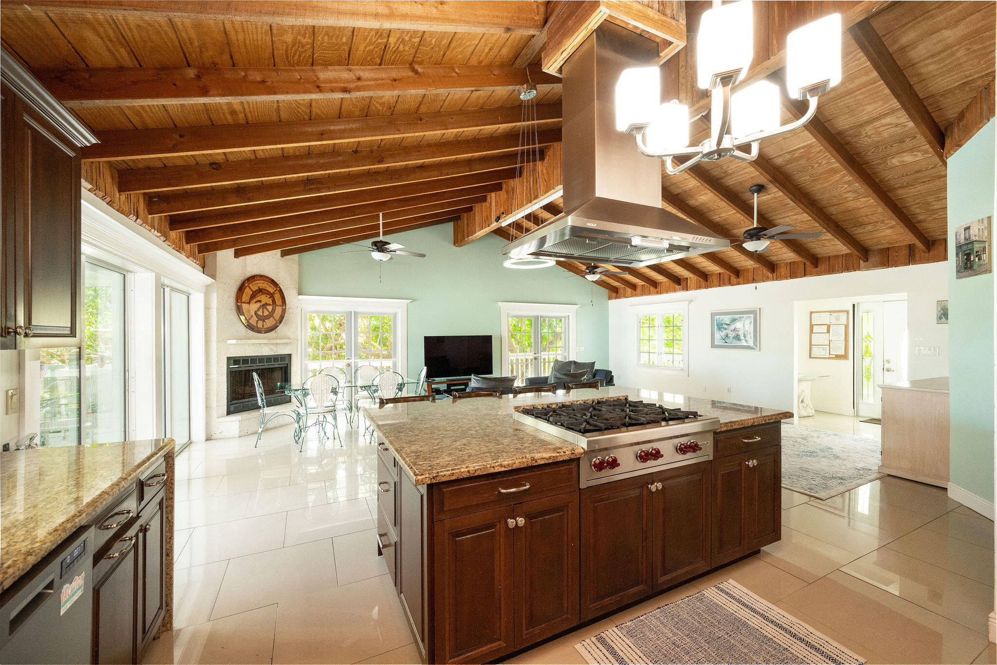 Open-plan kitchen with a large granite island beneath a vaulted wood-beam ceiling.