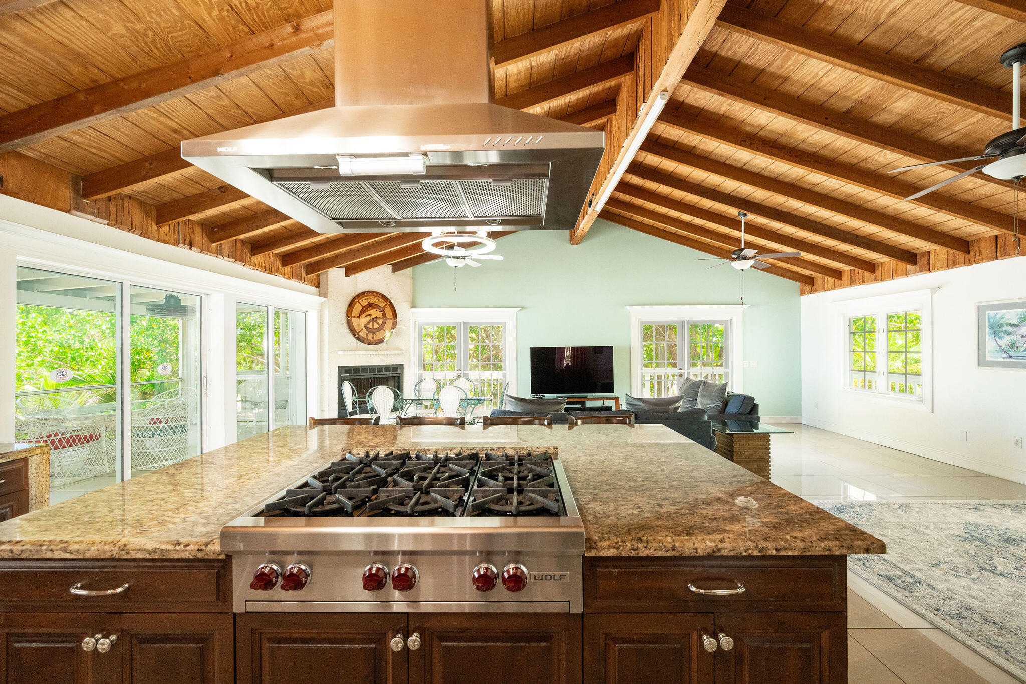 Open kitchen with granite island and Wolf range beneath an exposed timber ceiling, looking into the living area.