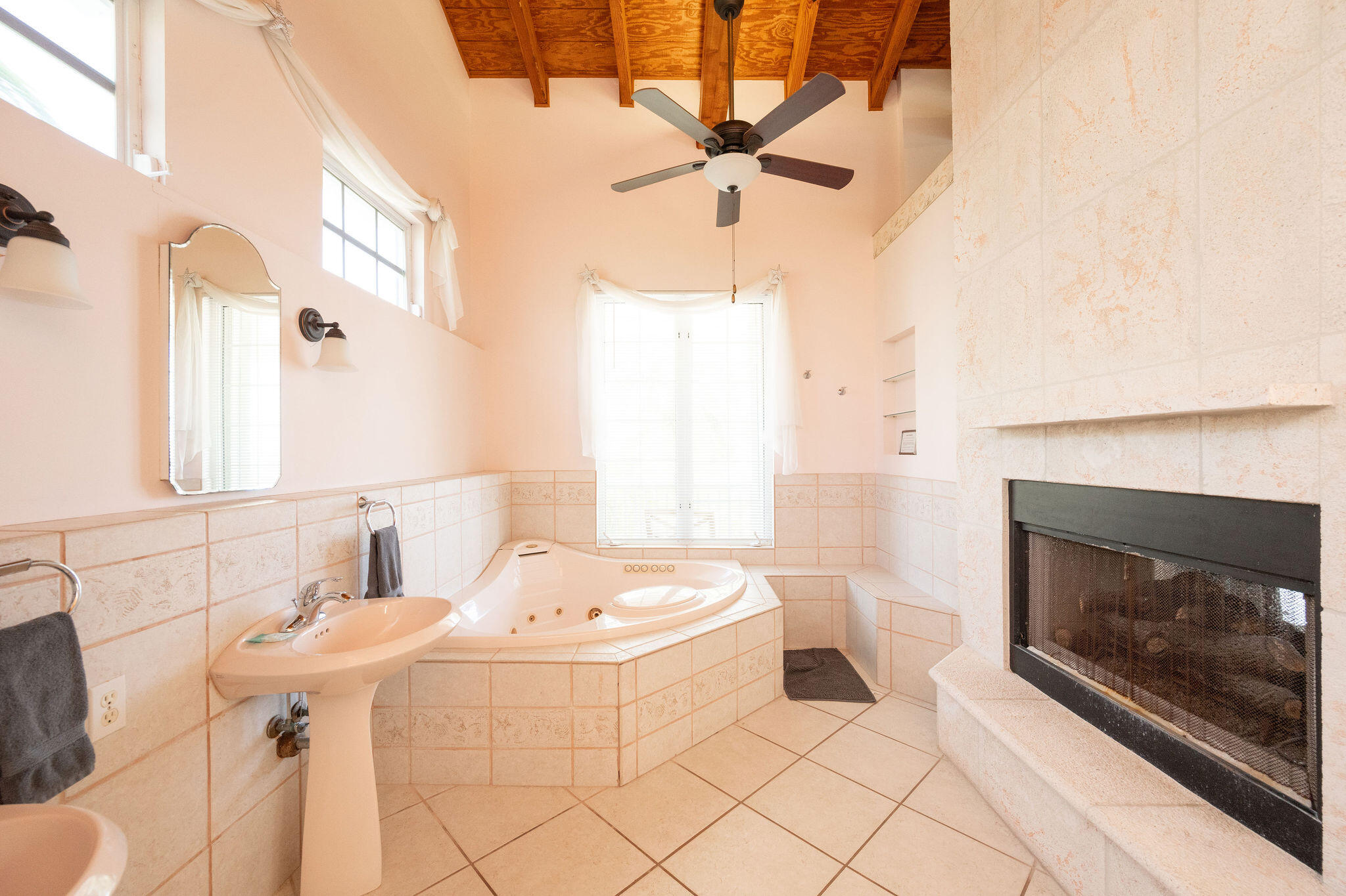 Bathroom with a corner whirlpool tub, tiled fireplace, and vaulted wood ceiling.