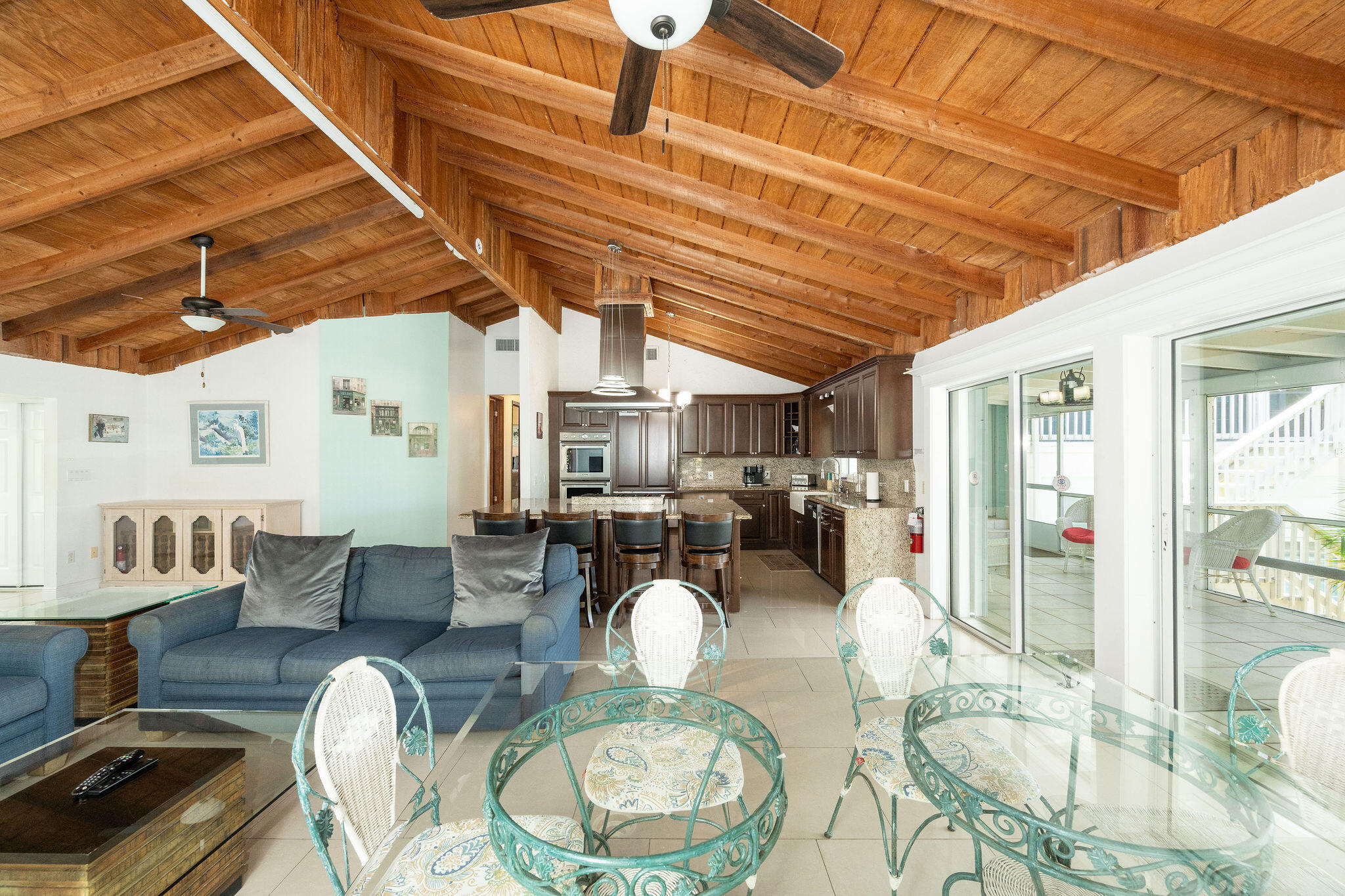 Open-plan living room and kitchen beneath a vaulted wood ceiling, with sliding doors to a patio.
