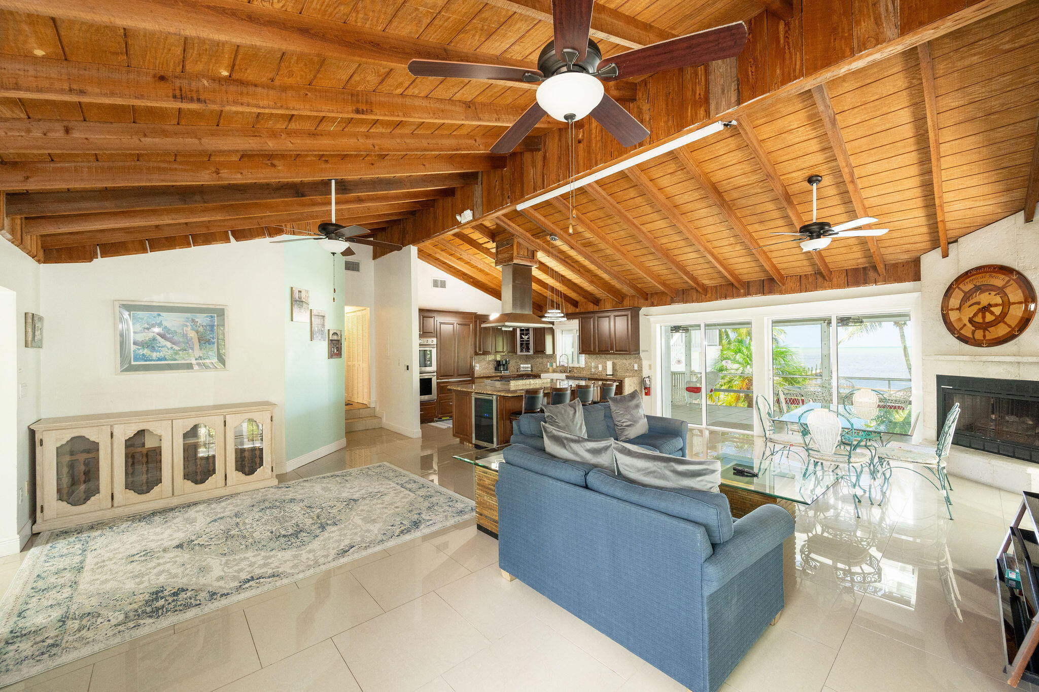Open-plan living room and kitchen with a vaulted wood ceiling and water views through glass doors.