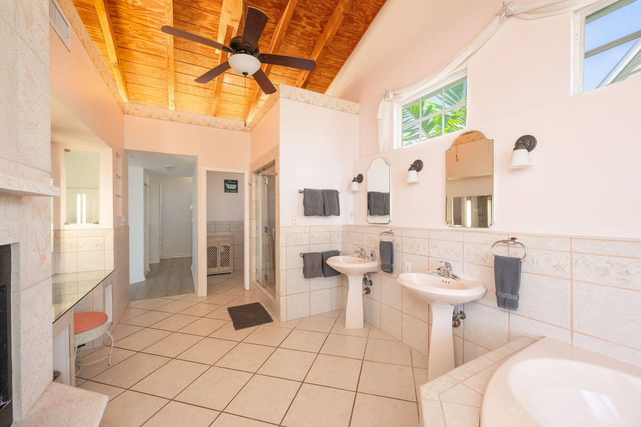 Spacious bathroom with double pedestal sinks, a glass shower, and a vaulted wood ceiling.
